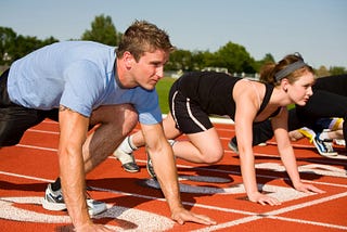 A man, a woman, and some other people outside of the camera frame, prepare themselves for a run on the racetrack.