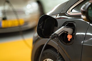 A picture of an electric car being charged. There is a grey charging nozzle sticking out of the charge port on the