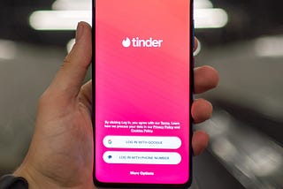 Person holding an open phone to the Tinder app login page