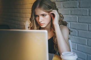 A beautiful girl with curly blond hair stares at her laptop.