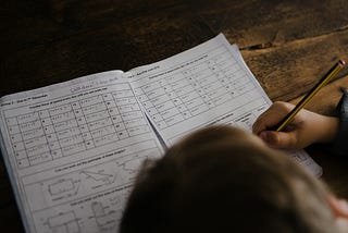 A child bent over their desk solving maths problems.