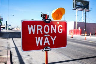 a wrong-way sign board on a road with a yellow light on it