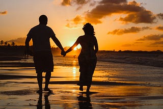 couple walking on the beach holding hands watching the sunset