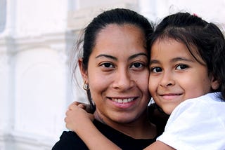 A woman smiling, holding a little girl who is smiling.