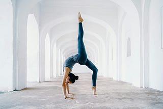 A woman doing a yoga pose in an empty hallway in an all-white building