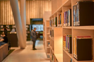 A bookshop with a modern design, and a man in the hazy background perusing the pages of an unknown book