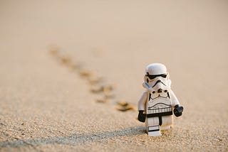 Photo by Daniel Cheung of a Lego Stormtrooper walking through the sand with footsteps behind him.