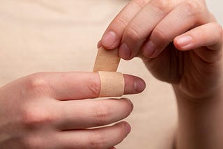 A left hand wrapping a band aid around a right forefinger