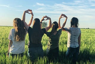 Four women standing in a field making hearts with their hands