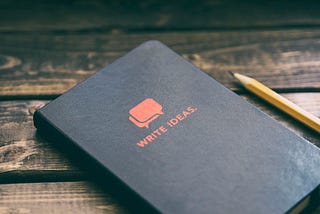 Black notebook labelled Write Ideas and a pencil on a wooden table