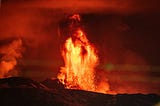 A fountain of orange-red lava shooting into the air during the nighttime.