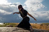 Blindfolded Woman Dancing on Top of a Rock