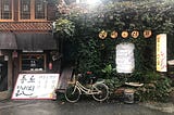 A bicycle is parked next to an ivy-covered wall in Seoul as the sun peaks over the roof of the building.