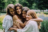 Four women hugging each other with flowers in the background