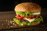 A large hamburger on a wooden table with pepper and sesame.