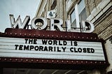 Marquee of an old theater with the word ‘WORLD’ in large letters on top. The sign below reads ‘The world is temporarily closed,’ referencing the global impact of the COVID-19 pandemic. The building has a classic, vintage aesthetic.