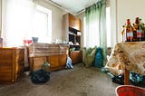 Room in house with old style furniture, cluttered surfaces and bagged up junk