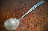 Large tarnished and scratched silver gravy ladle against a wood background.