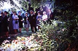 A line of people at a funeral standing behind a show of flowers