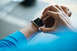 Close-up of a person wearing a smartwatch and adjusting the settings on its screen. The smartwatch displays the time as 5:42 and shows additional information, including steps taken and weather details.