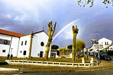 A white church with trees and a rainbow on the background.