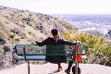 A man sitting on a bench looking out over a vista.