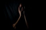 Woman’s face hidden by hands as she is scared, in the dark.