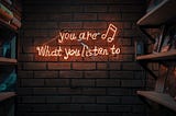 A brick wall with ‘you are what you listen to’ and a music bar with two notes in neon.