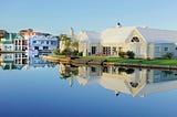 A neighborhood of elaborate mansions reflected in a large pond or lake.