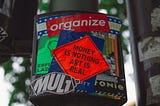 A protest sticker that says, “Money is nothing art is real.”