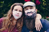 A man and a woman wearing masks that make them appear to be smiling, but their eyes convey how tired they actually are.