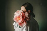 A woman with her face obscured by a bouquet of pink peonies.