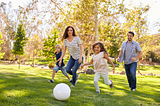 Family playing soccer in park together