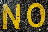 The word No painted in big, yellow letters on black asphalt