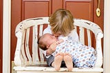 A boy sitting on a chair holding and kissing a baby.