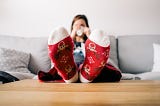 Woman sitting on a couch, drinking coffee, with sock-covered feet up on the coffee table.