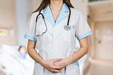 Close-up view of the torso of a medical professional with stethoscope standing with crossed arms. We don’t see the physician’s face.