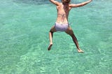 The author is jumping off a pier into clear, blue water.