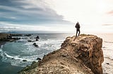 Man stands on a cliff overlooking ocean waters.