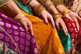 several women sitting in beautiful clothes from India, wearing gold bracelets