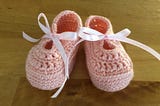 Pink, crocheted baby booties tied with pink ribbons.