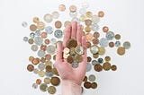 A hand holding coins, with many different coins on a white background