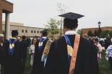 A view from the back of a college graduate in cap and gown, with other graduates in the background.