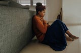 Anxious woman in orange sweater sitting on floor