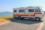 Old RV in a parking lot; alt-text for “I Had the Best Night’s Sleep in a Cracker Barrel Parking Lot”