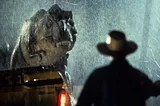 The silhouette of Dr. Allen Grant stands in front of a T. Rex in the rain.