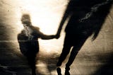 Shadows on pavement cast by a child and an adult holding hands as they walk.