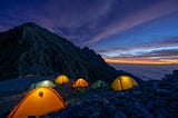 A picture of a campsite at nightfall, with several brightly-colored tents illuminated from within.