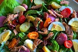 A plate piled high with a vibrant salad containing ingredients like sliced boiled eggs, cherry tomatoes, and shreds of meat.