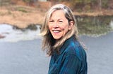 A woman standing near water outside, smiling